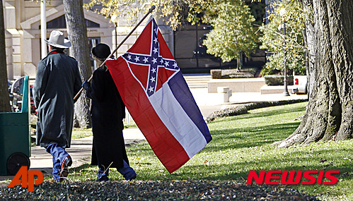 【잭슨( 미 미시시피주) = AP/뉴시스】= 미시시피주의 주도 잭슨의 주의사당 앞에서 지난 19일 미시시피주 깃발을 지지하는 시위를 마친 뒤 깃발을 들고 가는 사람들.  남부연합 깃발이 마지막으로 남아있는 미시시피주에서는 상단의 남부연합기를 즉시 제거하라는 의원들과 이 기를 걸지 않으면 처벌해야한다는 의원들이 대립하고 있다.     