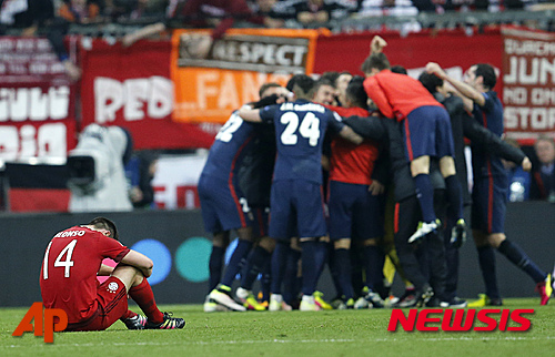 Bayern's Xabi Alonso sits on the pitch as Atletico players celebrate after advancing to the final after the final whistle of the Champions League second leg semifinal soccer match between Bayern Munich and Atletico de Madrid in Munich, Germany, Tuesday, May 3, 2016. (AP Photo/Michael Probst)