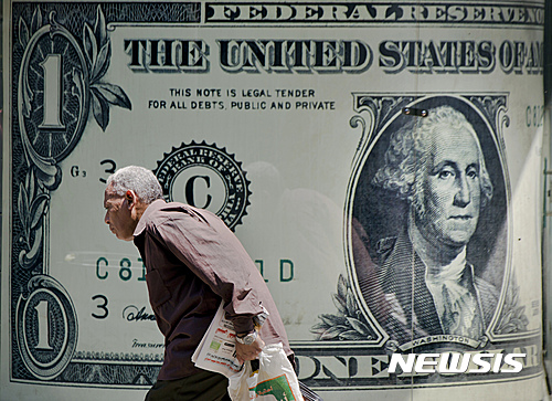A man walks past a poster showing a US dollar outside an exchange office in Cairo, Egypt, Wednesday, Aug. 17, 2016. Egypt's economy has been struggling since the 2011 uprising that overthrew longtime autocrat Hosni Mubarak, with high inflation, foreign currency shortages, and lack of tourism and investment that has hit both business and the broader population. (AP Photo/Amr Nabil)
