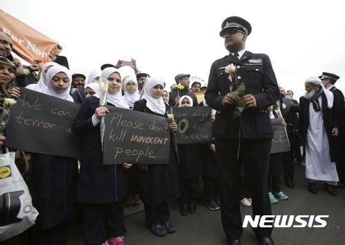 【런던=AP/뉴시스】29일(현지시간) 영국 런던 테러 일주일을 맞아 사건이 발생한 웨스트민스터 다리에서 추모 행사가 진행되고 있다. 사진은 추모식에서 무슬림 여학생들과 경찰관이 나란히 서있는 모습. 2017.3.30 