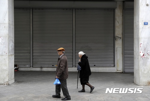 【아테네(그리스) = AP/뉴시스】 = 아테네의 닫혀진 은행 문 앞을 지나가는 노인 부부. 고령자가 많은 그리스에서는 경제난으로 인해 독거노인의 죽음과 사후처리가 문제가 되고 있다.  