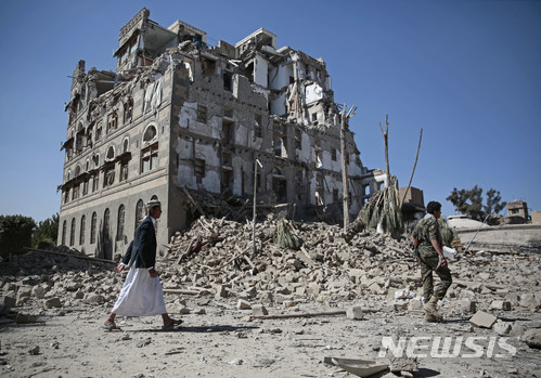 【사나=AP/뉴시스】지난 6일(현지시간) 예멘 수도 사나에서 후티 반군이 사우디 아라비아 공습으로 무너진 건물 앞을 걸어가고 있다. 2017.12.20.