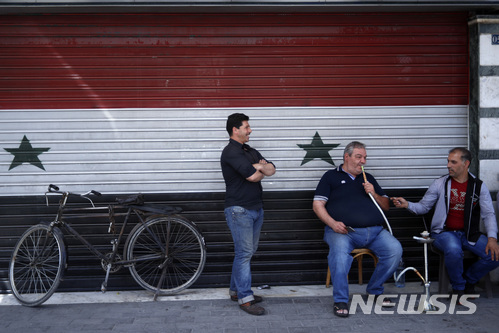 【다마스쿠스=AP/뉴시스】17일(현지시간) 시리아 수도 다마스쿠스의 한 상점 앞에 주민들이 앉아 있다. 상점 셔터는 시리아 국기 문양으로 장식돼 있다. 2018.4.18. 