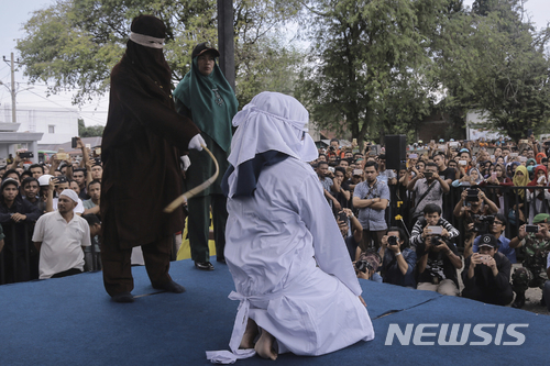 [반다아체(인도네시아)=AP/뉴시스] 인도네시아 반다아체에서 2018년 4월20일 군중들이 지켜보는 가운데 한 샤리아 집행관이 성매매를 한 여성 한 명에게 채찍질을 하고 있다. 2018.4.20