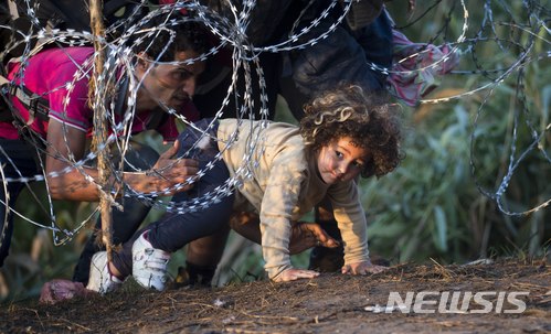 【루스케(헝가리)=AP/뉴시스】지난 2015년 8월27일 헝가리 남부 루스케에서 한 어린 소녀가 다른 사람의 도움을 받아 세르비아와의 국경지대에 설치된 철조망을 통과하고 있다. 헝가리 정부는 29일 헝가리가 이주자들의 나라가 되는 것을 막기 위한 헌법 개정과 이민 규제 강화 법안을 제안했다. 2018.5.30