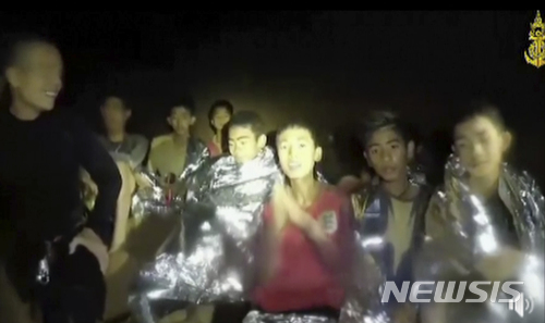 【태국 해군·AP/뉴시스】 태국 동굴에 실종됐던 소년들이 두 손을 합장하면서 자신들의 안부를 전하고 있다. 사진은 태국 해군이 4일 공개한 동영상을 캡처한 것이다. 왼쪽의 성인 남성은 태국 특수부대 네이비실 소속 잠수부로 추정된다. 2018.07.04 