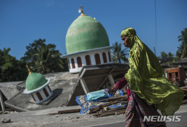 【강가(인도네시아 롬복섬)=AP/뉴시스】한 무슬림 여성이 지난 11일 인도네시 롬복섬의 강가에서 지난 5일 강진으로 무너진 이슬람 사원 앞을 지나가고 있다. 인도네시아 국가재난국은 13일 이번 지진으로 인한 사망자 수가 436명으로 늘었으며 재산피해도 최소 5조 루피아(3880억원)에 달하는 것으로 잠정 집계됐다고 말했다. 2018.8.13