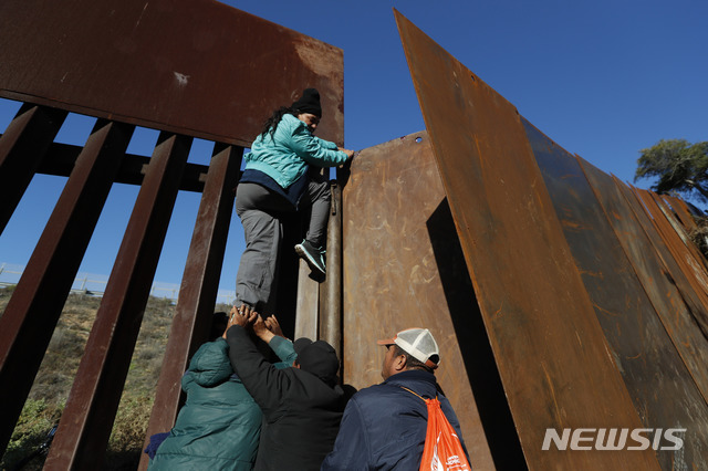 【티후아나=AP/뉴시스】12일(현지시간) 한 여성 온두라스 이민자가 동료들의 도움으로 멕시코 티후아나의 멕시코-샌디에이고 장벽을 넘고 있다. 시간이 오래 걸리는 망명 신청 절차를 피하려는 이들은 장벽을 넘어 미국 국경 경비대에 자수해 망명 절차를 밟는다. 2018.12.13.