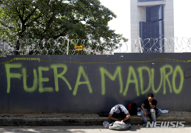 【카라카스=AP/뉴시스】20일(이하 현지시간) 베네수엘라 카라카스에서 스페인어로 "마두로 퇴진"이라고 적힌 보안 울타리 앞에 앉아있는 한 남성이 인근 중국 식당에서 얻은 음식물 쓰레기 봉지를 뒤지고 있다. 도널드 트럼프 미국 대통령은 22일 마두로 대통령 축출을 위해 베네수엘라에 더 가혹한 제재를 가할 수 있다고 밝혔다. 2019.03.21.