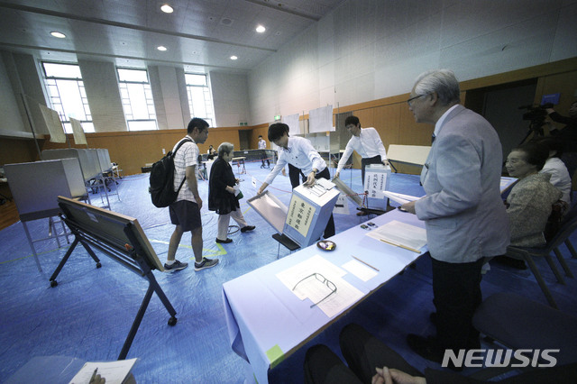 Representatives of a local election administration commission show two earliest voters the empty ballot box before they cast their votes for the upper house elections at a polling station in Tokyo Sunday, July 21, 2019. Voting started Sunday morning for the upper house elections where Japanese Prime Minister Shinzo Abe’s ruling coalition is seen to retain majority, according to local media report. (AP Photo/Eugene Hoshiko)