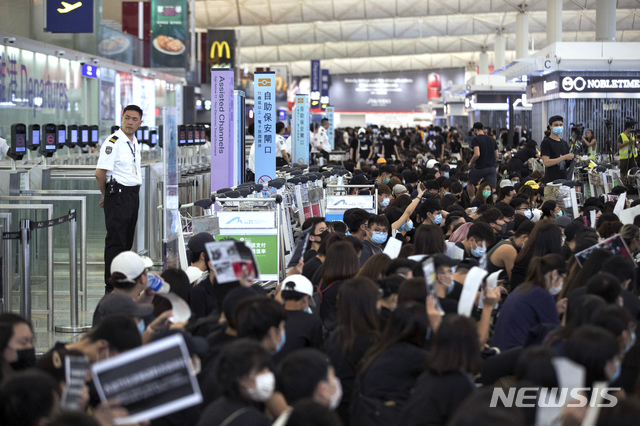 【홍콩=AP/뉴시스】 홍콩 국제공항에서 13일 2층 출국 홀을 점거한 시위대가 수하물 카트를 몰고와 출국 게이트 앞을 봉쇄한 가운데 한 공항 보안요원이 게이트 앞에서 뒷짐 지고 이를 보고 있다. 이날 공항 당국은 시위대가 1층 입국장과 2층을 다시 점거하자 2층의 항공사 체크인 서비스를 오후 5시 무렵 전면 중단했다. 시위대가 출국 게이트를 막아선 것은 그 다음 상황으로 보인다. 2019. 8. 13. 