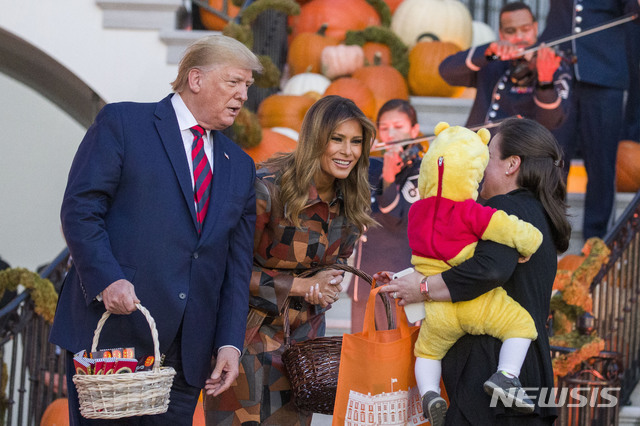  【워싱턴=AP/뉴시스】도널드 트럼프 미국 대통령과 부인 멜라니아 여사가 28일(현지시간) 핼러윈 장식을 한 백악관 사우스 론에서 엄마에게 안긴 한 어린이에게 핼러윈 사탕을 나눠주고 있다. 2019.10.29. 