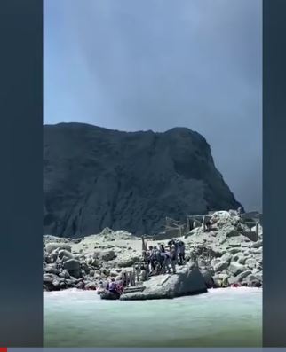 [서울=뉴시스] 뉴질랜드 화이트 아일랜드에서 9일 화산이 분출한 후 현지에 있던 관광객들이 구조 보트를 타기 위해 해안가 돌 위에 서있다. 이번 분출로 최소 13명이 사망한 것으로 잠정 집계됐다. <사진출처: TVNZ 동영상 화면 캡처> 2019.12.10 