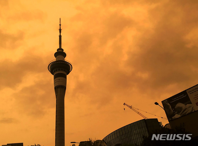 [오클랜드=AP/뉴시스] 뉴질랜드 오클랜드 스카이 타워 뒤로 5일 오렌지 색으로 변한 하늘이 보이고 있다. 호주 산불사태로 인한 연기로 하늘이 오렌지 빛이 됐다. 2020.01.07