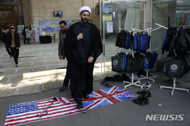 [테헤란=AP/뉴시스]14일(현지시간) 이란 수도 테헤란의 테헤란 대학교에서 지난 3일 미국의 드론 공격으로 이라크에서 사망한 솔레이마니 쿠드스군 총사령관 추모식이 열린 가운데 한 성직자가 추모식을 마치고 돌아가며 미국과 영국 국기를 밟으며 지나가고 있다. 2020.01.15.