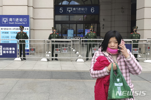 [우한=AP/뉴시스] 폐렴이 강타한 중국 우한에서 23일 봉쇄령으로 기차역이 폐쇄된 가운데 한 여성이 휴대전화통화를 하며 경찰들 앞을 지나가고 있다. 2020.01.24.