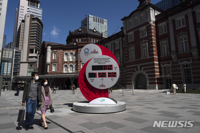 [도쿄=AP/뉴시스]12일 한 남녀가 일본 도쿄 거리에 설치된 2020 도쿄 올림픽 카운트다운 시계 옆을 지나가고 있다. 2020.03.12.