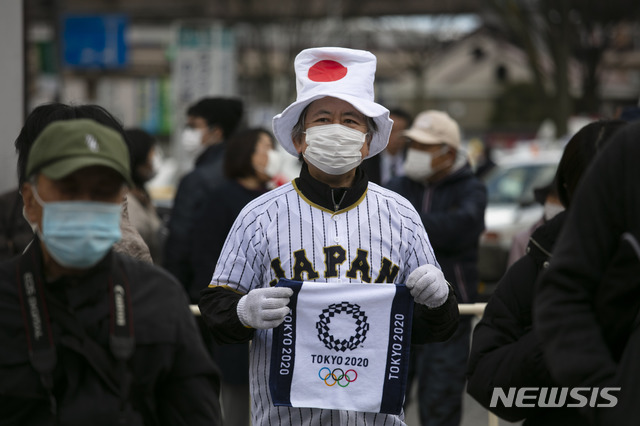 [후쿠시마=AP/뉴시스]24일 일본 후쿠시마에서 올림픽 성화가 일반에 공개돼 사람들이 모여든 가운데 일본 국기 모양의 모자를 쓴 한 남성이 올림픽 기념 수건을 들고 있다. 도쿄올림픽·패럴림픽 조직위원회는 오는 26일의 성화 봉송을 주자가 아닌 차량으로 봉송하는 방안을 고려하고 있다고 밝혔다. 2020.03.24.