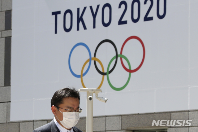 [도쿄=AP/뉴시스]25일(현지시간) 일본 도쿄도청에 걸린 2020 도쿄올림픽 로고 앞을 한 행인이 마스크를 쓰고 걸어가고 있다. 오는 7월 예정돼 있던 도쿄올림픽은 신종 코로나바이러스 감염증(코로나19) 여파로 내년으로 연기됐다. 2020.3.25.