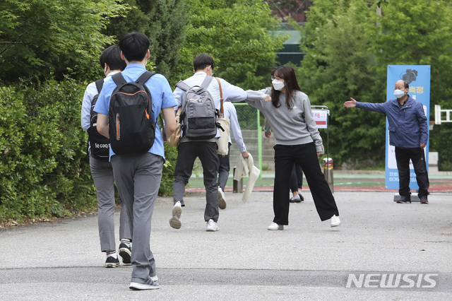 A senior student is greeted by a teacher, second from right, upon his arrival at the Kyungbock High School in Seoul, South Korea, Wednesday, May 20, 2020. South Korean high schools reopened on Wednesday after weeks of postponement due to safety concerns over the coronavirus outbreak. (AP Photo/Ahn Young-joon)
