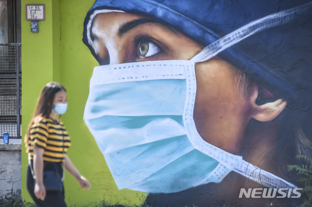 [밀라노=AP/뉴시스]21일(현지시간) 이탈리아 밀라노의 사코병원 벽에 신종 코로나바이러스 감염증(코로나19)과 싸우는 이 병원 의료진에 헌정하는 벽화가 그려져 마스크를 쓴 한 여성이 그 앞을 지나고 있다. 2020.07.22.