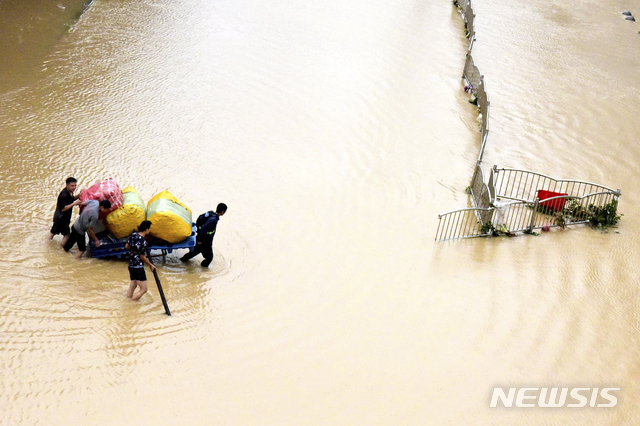 [정저우=AP/뉴시스] 21일 중국 허난성 정저우에서 시민들이 귀중품 등을 수레에 싣고 침수 거리를 건너고 있다. 중국군은 정저우 인근 댐이 홍수로 균열이 생기자 수압을 낮추기 위해 제방을 폭파하기도 했다. 지금까지 홍수로 최소 25명이 숨지고 7명이 실종된 것으로 알려졌다. 2021.07.22.