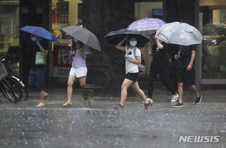 [타이베이=AP/뉴시스] 제14호 태풍 찬투가 대만섬 동해안을 스쳐간 12일 수도 타이베이 시내에서 코로나19 예방을 위해 마스크를 착용한 시민들이 우산을 쓴 채 걸어가고 있다. 2021.09.12