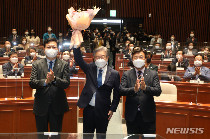 [서울=뉴시스] 전신 기자 = 이재명 더불어민주당 대선후보가 15일 서울 여의도 국회에서 열린 의원총회에서 윤호중 원내대표로부터 받은 꽃다발을 들고 있다. (공동취재사진) 2021.10.15. photo@newsis.com