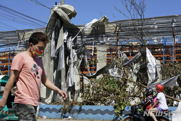 [세부=AP/뉴시스] 20일(현지시간) 필리핀 중부 세부에서 주민들이 태풍 '라이'로 인해 날아든 금속판이 뒤덮은 전신주 주변을 지나가고 있다. 필리핀 경찰은 제22호 태풍 라이로 375명이 숨진 것으로 집계됐다고 발표하면서 통신망이 복구되면 파악되는 피해 상황은 더 늘어날 것이라고 밝혔다. 2021.12.21.