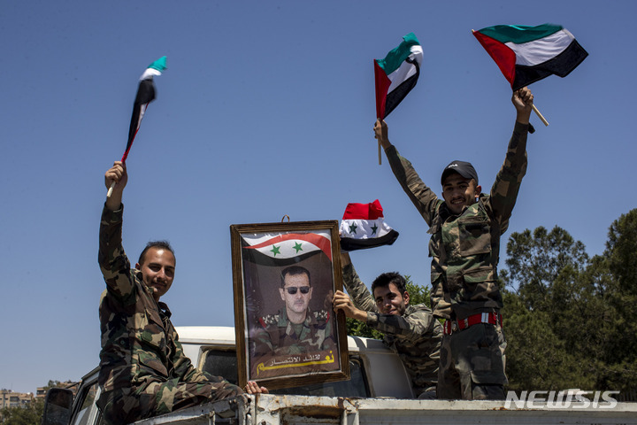 [다마스쿠스(시리아)=AP/뉴시스] 시리아 군인들이 지난해 5월26일 시리아 수도 다마스쿠스 인근 동부 구타 지역에서 바트당 깃발과 "승리의 지도자에게 예스"라고 적힌 바샤르 아사드 시리아 대통령의 초상화를 들고 웃고 있다. 블라디미르 푸틴 러시아 대통령은 지난 11일 중동 출신 민병대들이 전투에 참여하는 것을 승인했다. 2022.03.15. *재판매 및 DB 금지