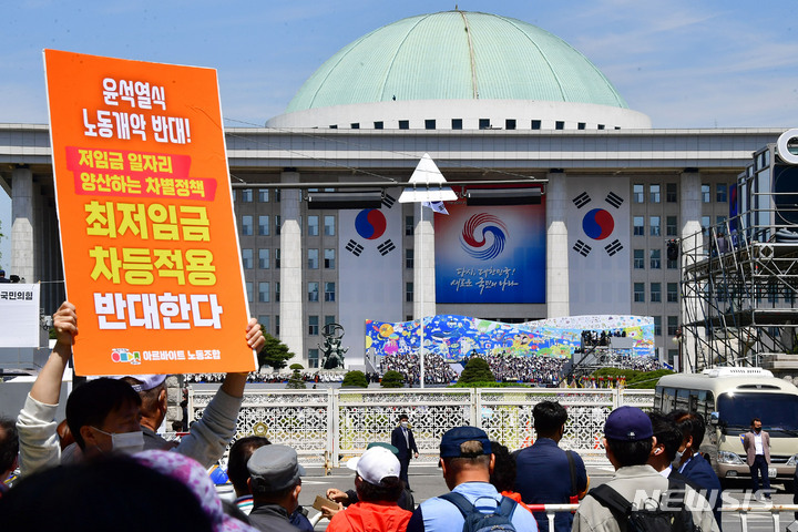 [서울=뉴시스] 전진환 기자 = 지난 10일 국회에서 제20대 대통령 취임식이 열린 가운데 국회 앞 도로에서 한 아르바이트 노조원이 '최저임금 차등적용 반대' 피켓을 들어보이고 있다. (공동취재사진) 2022.05.10. photo@newsis.com