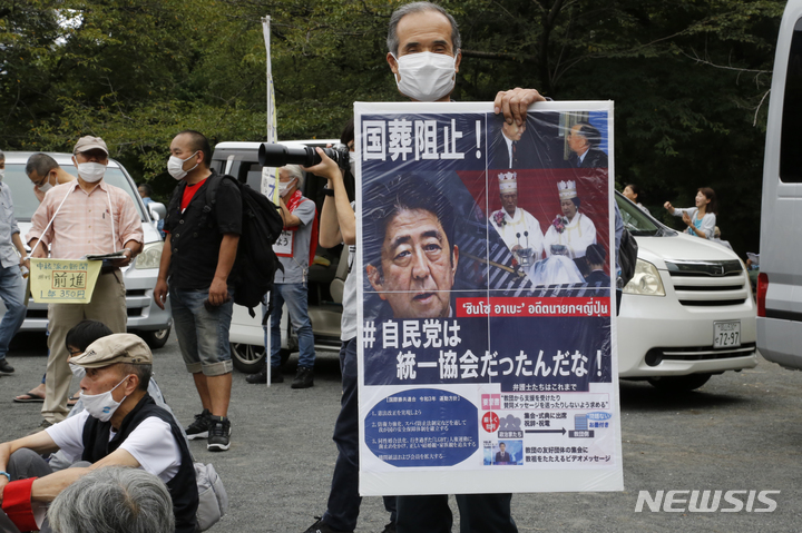 [도쿄=AP/뉴시스] 23일 일본 도쿄의 한 공원에서 한 남성이 아베 신조 전 일본 총리의 국장에 반대하는 포스터를 들고 시위에 참여하고 있다. 2022.09.23.