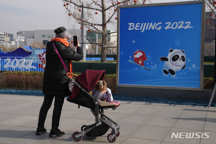 [서울=AP/뉴시스] 영국의 한 여성이 '강아지가 탄 유모차'를 위해 2살 아이가 탄 유모차를 접어달라는 요구를 받았다. 사진은 지난해 1월18일 유모차에 강아지를 태운 중국의 한 여성이 2022 베이징 올림픽 포스터 앞에서 사진을 찍고 있는 모습. *재판매 및 DB 금지