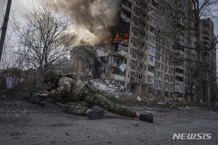 [아우디이우카=AP/뉴시스] 지난 17일(현지시간) 우크라이나 아우디이우카에서 한 경찰관이 러시아군의 공습으로 불타는 건물 주변으로부터 몸을 피하고 있다. 2023.03.21.