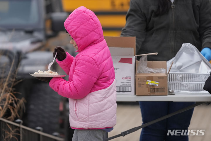 [시카고=AP/뉴시스]시카고시의 이민 혹한대피소 난방 버스앞에서 한 이민어린이가 자원봉사자들에게서 배급받은 음식을 먹고 있다. 2024.01.18. 