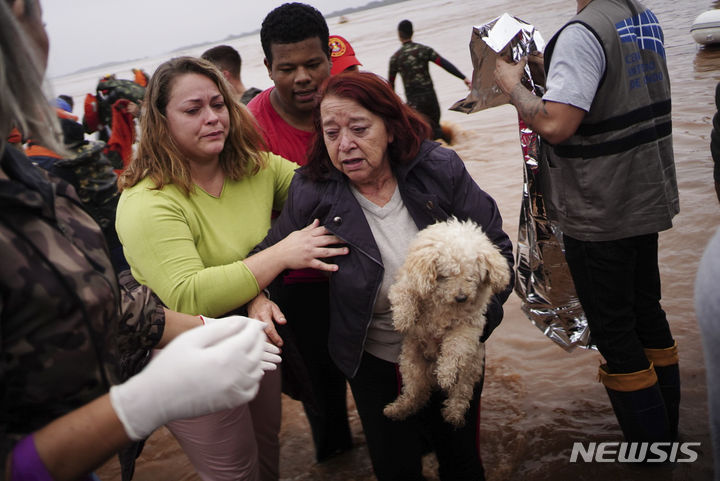 [리우그란데두술=AP/뉴시스] 폭우로 인해 홍수가 발생한 4일(현지시각) 브라질 남부 리우그란데두술주 포르투 알레그레에서 한 여성이 강아지를 안고 대피하고 있다. 2024.05.07.