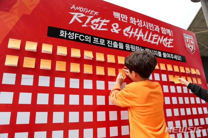 [화성=뉴시스] 화성FC의 프로 추진을 응원하는 어린이 팬이 메시지 보드에 응원문구를 붙이고 있다.(사진=화성FC제공)2024.05.10.photo@newsis.com