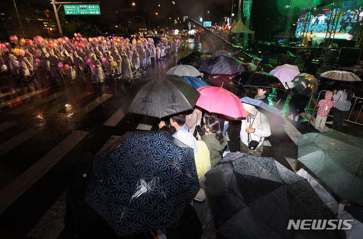 [서울=뉴시스] 김명년 기자 = 부처님오신날을 앞둔 11일 오후 서울 종로 일대에서 관람객들이 우산을 쓰고 연등 행렬을 구경하고 있다. 2024.05.11. kmn@newsis.com