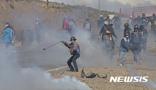 【판두로(볼리비아)=AP/뉴시스】파업을 벌이고 있는 볼리비아 광부들이 25일 판두로에서 시위 중 최루탄을 쏘며 진압에 나선 경찰을 향해 돌을 던지며 맞서고 있다. 볼리비아 언론들은 로돌포 일라네스 볼리비아 내무부 차관이 25일 파업 중인 광부들에게 납치됐다가 이들에게 맞아 사망했다고 보도했다. 2016.8.26
