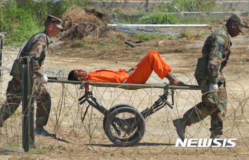 【 AP/뉴시스】 = 쿠바의 관타나모 만에 있는 미해군기지 않의 악명높은 미군감옥에서 미군들이 2002년 아프간출신의 재소자를 들것에 싣고 군사법정으로 이송하는 장면. 트럼프는 이 감옥을 재사용하려 하고 있으며 오바마의 백악관은 지난 1월 17일 이 교도소가 아직도 문을 열고 있어 버락 오바마대통령의 폐쇄계획이 실패했음을 시인했다.   