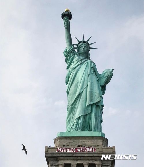【AP/뉴시스】미국 뉴욕에 위치한 자유의 여신상 아래 부분에 '난민을 환영합니다'(Refugees Welcome)라는 문구가 적힌 대형 현수막이 걸려 있다. 2017.2.22.