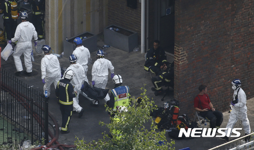 【런던=AP/뉴시스】영국 런던 고층아파트 화재현장에서 14일(현지시간) 경찰 소속 법의학 팀원들이 사망자가 실려 있는 것으로 보이는 들것을 옮기고 있다. 2017.06.15