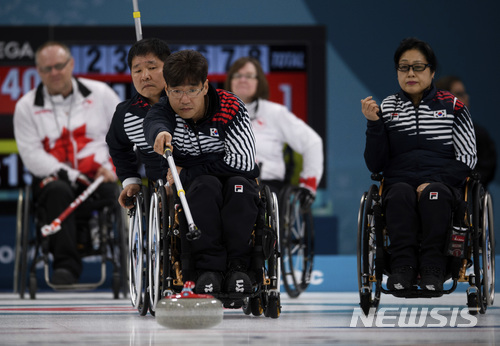 South Korean Soonseok Seo delivers a stone while Dongha Lee, left, and Min-Ja Bang, right, look on during the Wheelchair Curling Bronze Medal Game between South Korea and Canada at the Gangneung Curling Centre in Gangneung, South Korea at the 2018 Winter Paralympics Saturday, March 17, 2018. (Joel Marklund/OIS/IOC via AP)