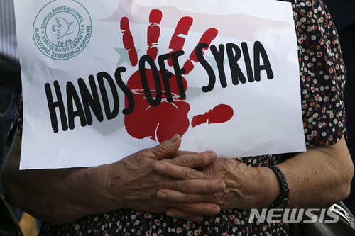 【니코시아=AP/뉴시스】16일(현지시간) 키프로스 니코시아에 위치한 미국 대사관 밖에서 미국 주도의 시리아 화학무기 시설 공습을 규탄하는 시위가 벌어지고 있다. 한 시위자가 '시리아에서 손 떼라'는 문구가 적힌 종이를 들고 있다. 2018.4.17. 