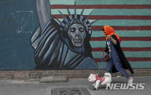 【테헤란(이란)=AP/뉴시스】한 이란 여성이 8일 반미 벽화가 그려진 테헤란의 전 미국 대사관 건물 앞을 애완견을 데리고 지나가고 있다. 이란 국회의원들은 9일 테헤란의 국회의사당에서 도널드 트럼프 미 대통령이 이란 핵협정에서 탈퇴한 것을 비난하며 "미국에 죽음을"이라는 구호를 외치면서 종이로 만든 미 성조기를 불태웠다. 2018.5.9