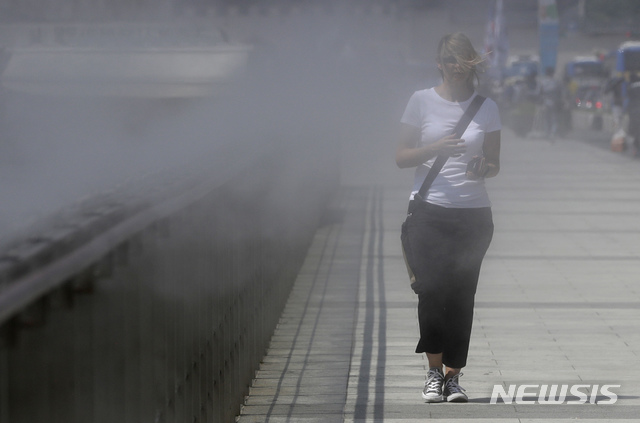 A visitor walks through a water mist to cool herself off at the Gwanghwamun Square in downtown Seoul, South Korea, Tuesday, July 17, 2018. South Korean Meteorological Administration issued a heat wave warning for Seoul and other cities. (AP Photo/Lee Jin-man) 