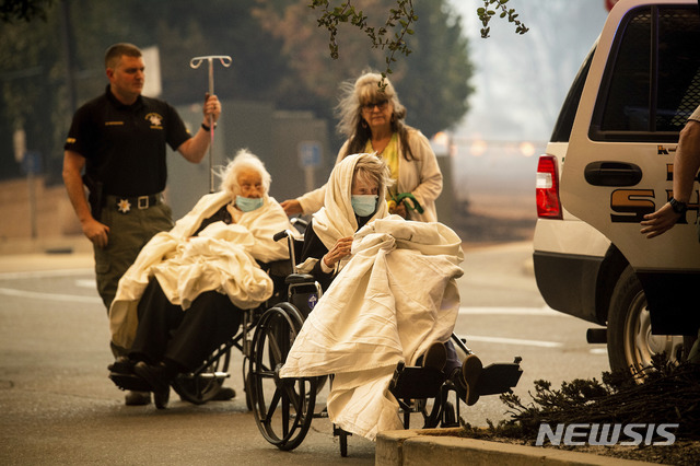 【파라다이스(캘리포니아)=AP/뉴시스】 8일(현지시간) 미국 캘리포니아 북부 뷰트 카운티 파라다이스 지역에서 대형 산불이 발생해 파라다이스 병원에 입원 중이던 환자 60명이 대피하고 있다. 이들 뒤로 화재로 인한 연기가 자욱하다. 2018.11.09.