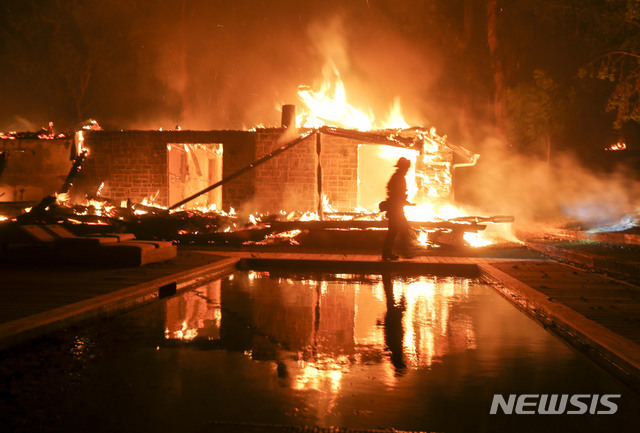 A firefighter walks by the a burning home in Malibu, Calif., Friday, Nov. 9, 2018. A Southern California wildfire continues to burn homes as it runs toward the sea. Winds are blamed for pushing the fire through scenic canyon communities and ridgetop homes. (AP Photo/Ringo H.W. Chiu)