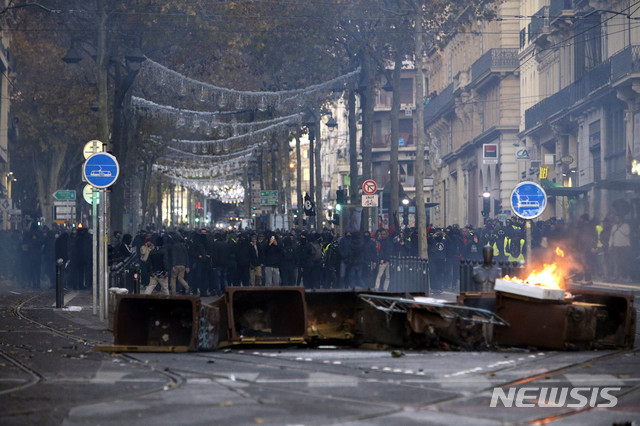 Demonstrators stand behind a burning bin during clashes, Saturday, Dec. 8, 2018 in Marseille, southern France. The rumble of armored police trucks and the hiss of tear gas filled central Paris on Saturday, as French riot police fought to contain thousands of yellow-vested protesters venting their anger against the government in a movement that has grown more violent by the week. (AP Photo/Claude Paris)