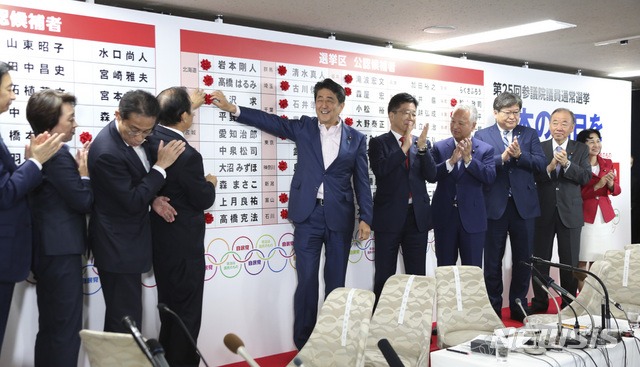 Japanese Prime Minister Shinzo Abe, center, smiles with his party&#039;s lawmakers in front of red rosettes on the names of his Liberal Democratic Party&#039;s winning candidates during ballot counting for the upper house elections at the party headquarters in Tokyo, Sunday, July 21, 2019. Prime Minister Abe&#039;s ruling coalition appeared certain to hold onto a majority in Japan&#039;s upper house of parliament, with exit polls from Sunday&#039;s election indicating he could even close in on the super-majority needed to propose constitutional revisions.(AP Photo/Koji Sasahara)
